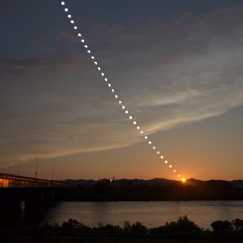 部分日食と夕映えの信濃川に沈む夏至の太陽